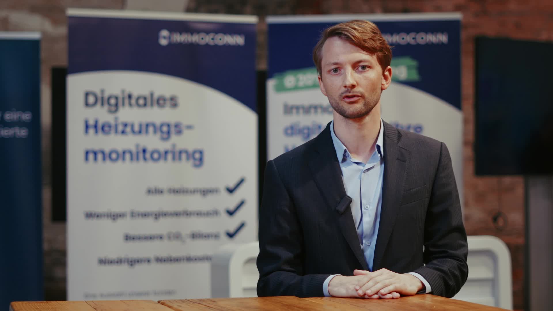 Mann in Anzug steht vor Bannern mit der Aufschrift ‚Digitales Heizungsmonitoring‘ und spricht vor Publikum